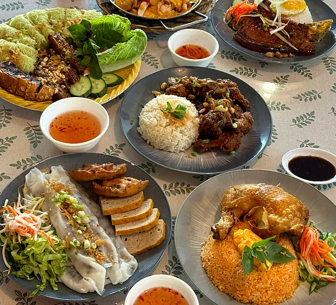 Table of Vietnamese dishes: rice with crispy chicken wings, steamed rice rolls, a grilled-meat noodle platter and crispy chicken on red fried rice