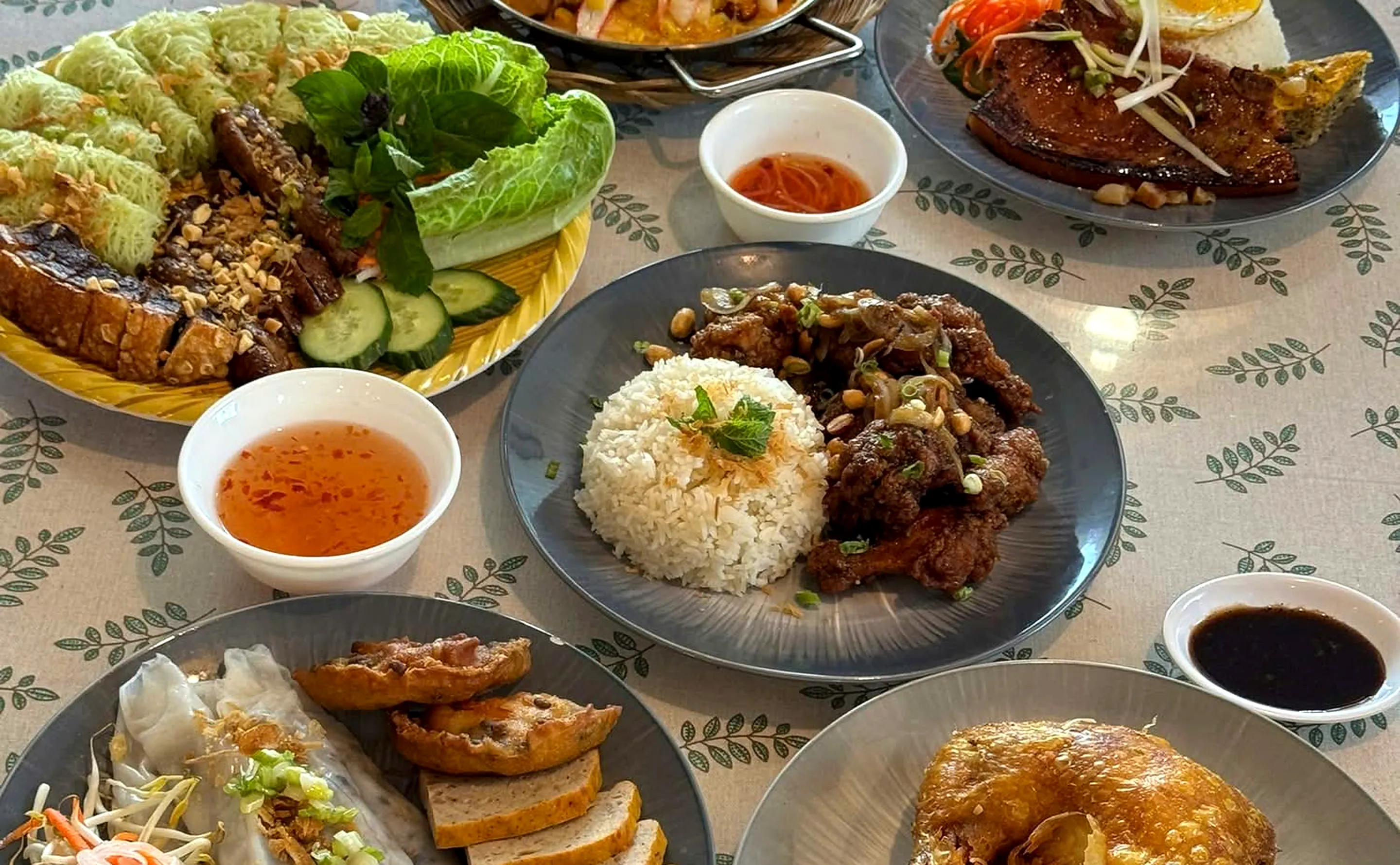 Table of Vietnamese dishes: rice with crispy chicken wings, steamed rice rolls, a grilled-meat noodle platter and crispy chicken on red fried rice