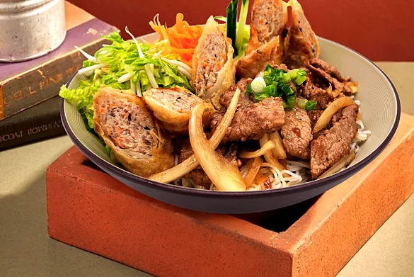 Rice vermicelli bowl topped with grilled pork, Vietnamese sausage and spring rolls