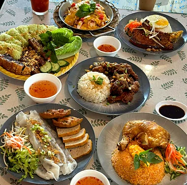 Table of Vietnamese dishes: rice with crispy chicken wings, steamed rice rolls, a grilled-meat noodle platter and crispy chicken on red fried rice