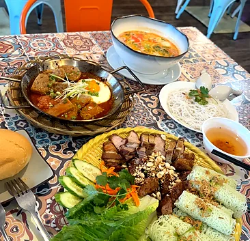 Vietnamese meatballs in tomato sauce with a fried egg in a small wok pan, baguette, soup and a grilled-meat platter
