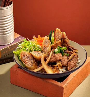Rice vermicelli bowl topped with grilled pork, Vietnamese sausage and spring rolls
