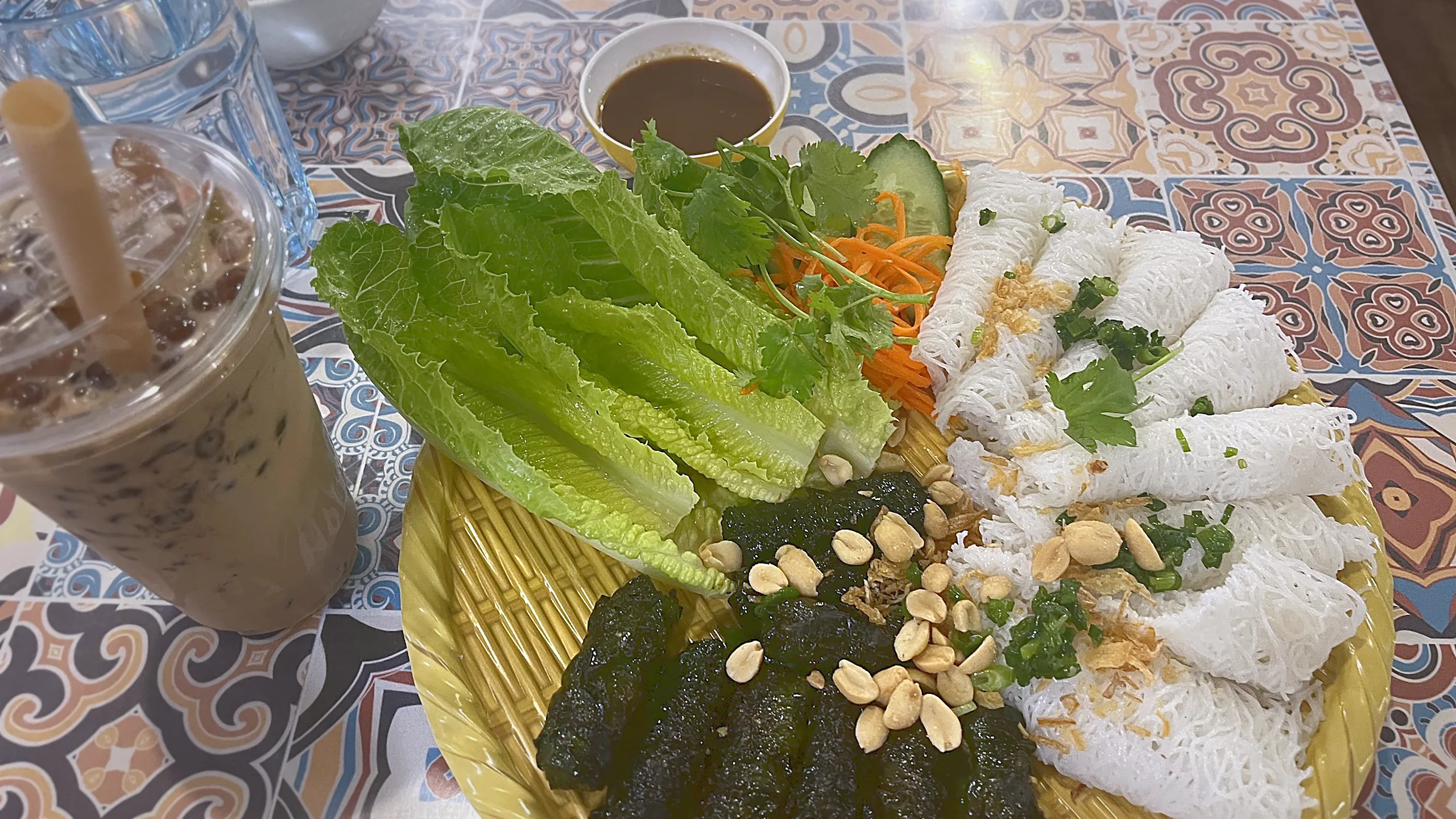 Woven rice vermicelli with grilled beef in betel leaves, lettuce, herbs and peanuts on a woven tray, with a milk tea