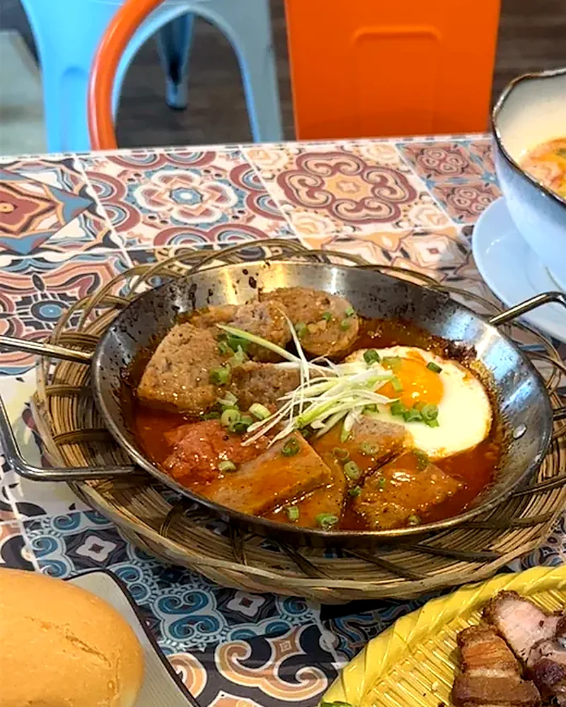 Vietnamese meatballs in tomato sauce with a fried egg in a small wok pan, served with a baguette
