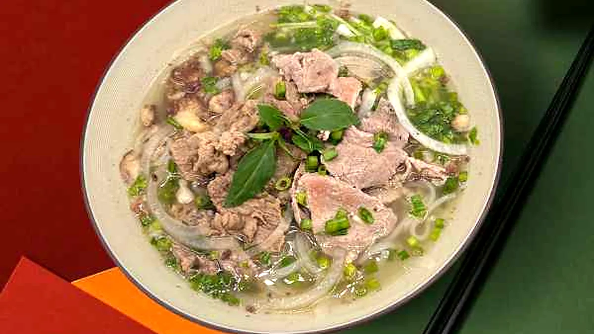 Bowl of rare beef pho with herbs and onions